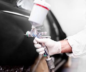 Worker using paint spray gun for painting a car